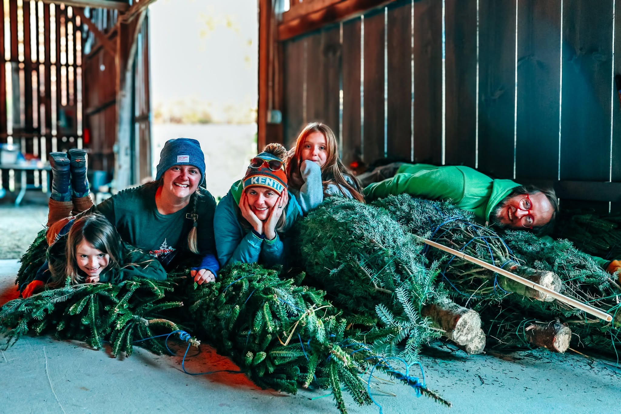Members of the Hutton-Loyd family laying on a pile of Christmas trees.
